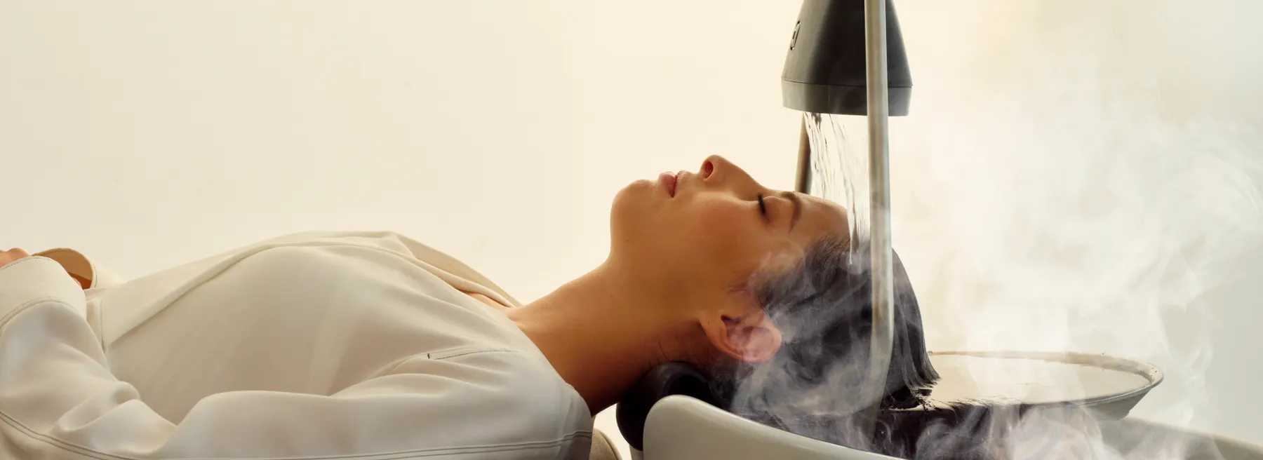 Une cliente allongée sur le bac YUME : la cascade d’eau chaude coule sur ses cheveux dans un nuage de brume